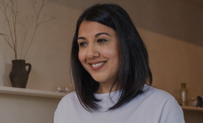 Woman pouring tea into a teapot in a modern kitchen, smiling and enjoying a peaceful moment.