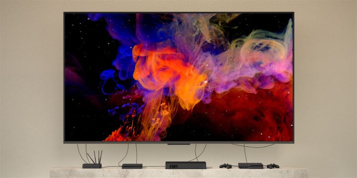 Close up of a QNED9M mounted on a wall connected to multiple devices. Wires and devices fade leaving just the QNED9M mounted on a wall. Zooms out to show the QNED9M mounted in a modern home. Zero Connect Box sits on a coffee table.