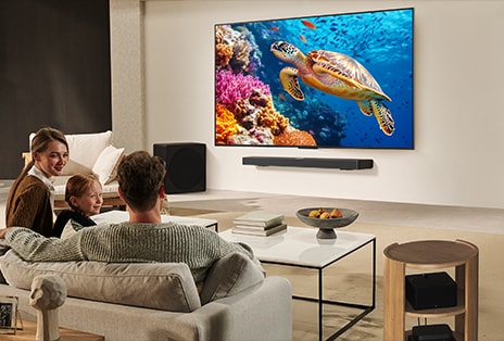 A family sits on a couch facing a LG TV mounted on a wall above a LG Soundbar. Zero Connect Box sits inside a coffee table.