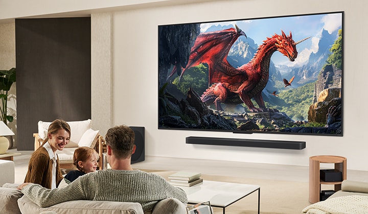 A family sits on a couch facing a LG QNED TV mounted on a wall above a LG Soundbar with a little girl pointing to a screen depicting two dolphins.