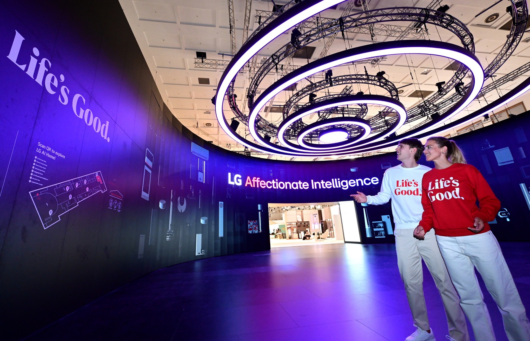 Two people wearing LG clothing standing in purple room with LGs AI Home on the walls