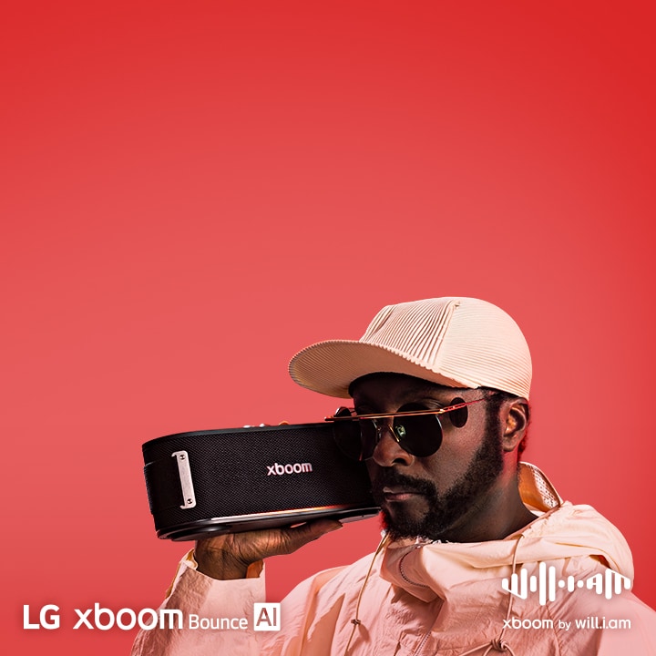 will.i.am in white outfit and sunglasses is holding xboom Bounce right next to his face.