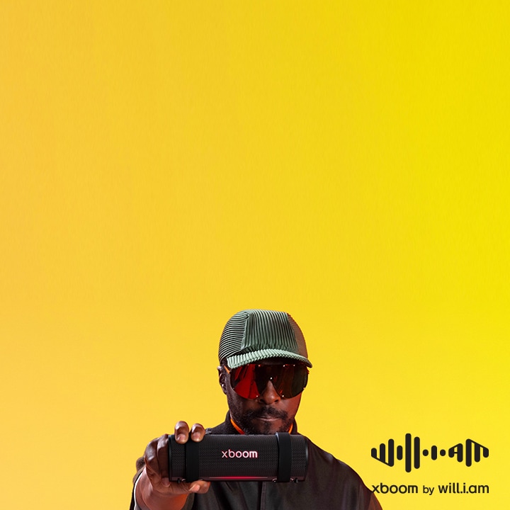 will.i.am trong trang phục đen cùng kính râm cá tính, khoác chiếc xboom Grab trên vai đầy phong cách.