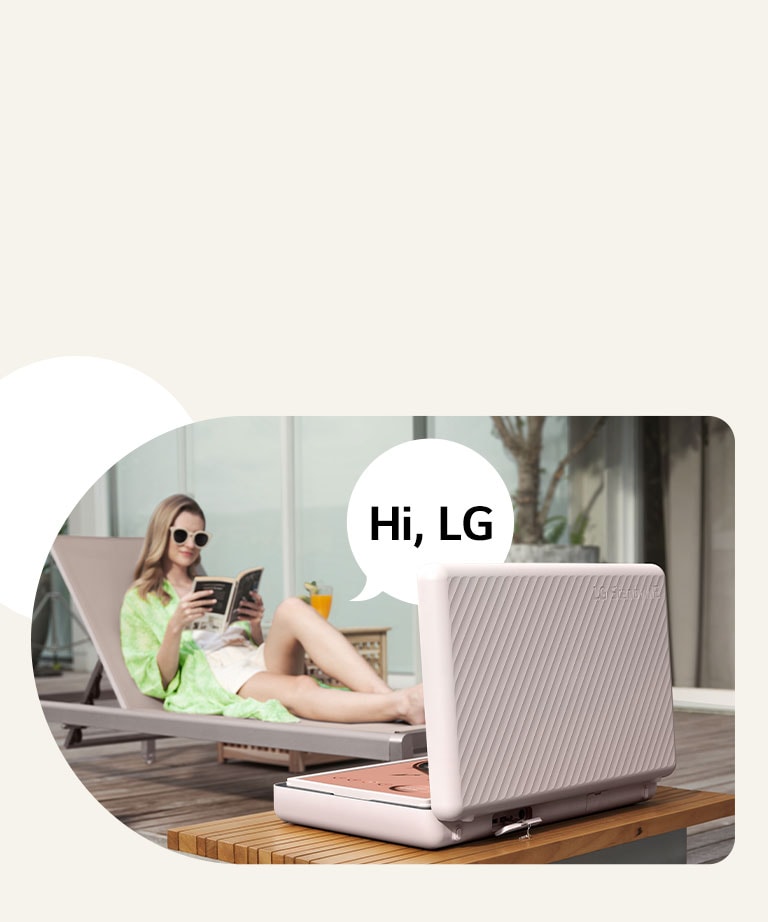 Mặt sau của LG StanbyME Go, TV đặt ngay trước bàn ngoài hiên. Một người phụ nữ đang thư giãn trên ghế bãi biển, điều khiển màn hình bằng giọng nói của mình.  Bong bóng thoại có dòng chữ "Hi, LG" được hiển thị ở bên phải cô ấy.