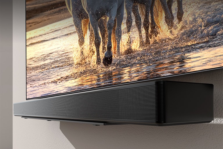 Màn hình TV hiển thị một con ngựa đang chạy trên bãi biển hoàng hôn và loa Soundbar treo trên tường cùng nhau.