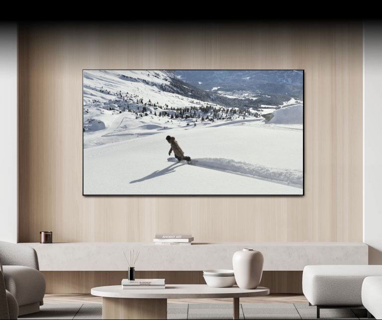 Trong phòng khách, một chiếc TV trên tường hiển thị video về một người đang trượt tuyết. Một bong bóng thông báo có nội dung "Gửi màn hình đến TV phòng ngủ" xuất hiện ở cuối màn hình, khiến TV tắt và video tiếp tục phát trên TV phòng ngủ. Một bong bóng thông báo khác có nội dung "Gửi màn hình đến TV phòng khách" xuất hiện, khiến video chuyển trở lại TV phòng khách và TV phòng ngủ sẽ tắt.