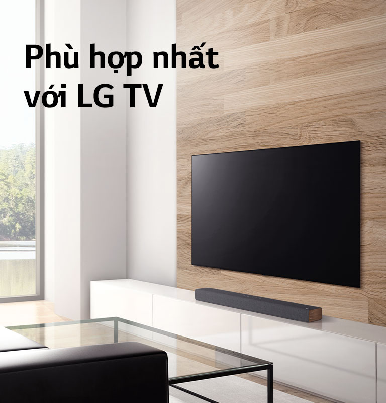 A soundbar is placed on a white TV cabinet and TV is placed on a wooden wall. There is a forest view outisde the window. Text is written on image - The Best Match with LG TVs.