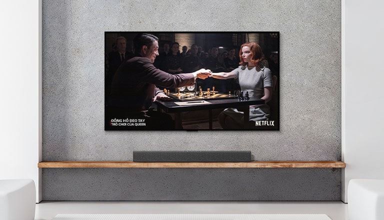 A soundbar and TV are in a white living room. A woman and a man are playing chess on TV screen.