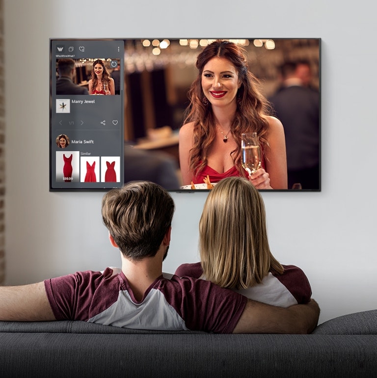 Cặp vợ chồng ngồi trên ghế dài xem TV hiển thị một người phụ nữ và thông tin sản phẩm của một chiếc váy đỏ mà người phụ nữ đang mặc.