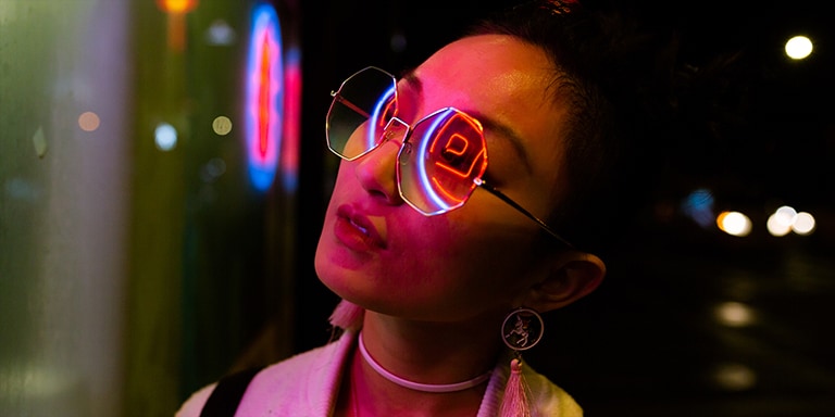 Cận cảnh một phụ nữ đeo kính râm với ánh đèn neon phản chiếu trên người