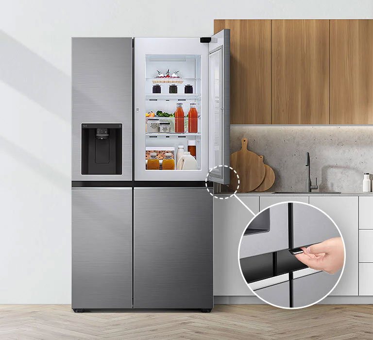 A front view of the refrigerator installed in a kitchen. The top right door is open and there is a circle and a line leading to a larger circle that shows a magnified view of the button on the bottom left corner of the open door which has a concealed opening button.