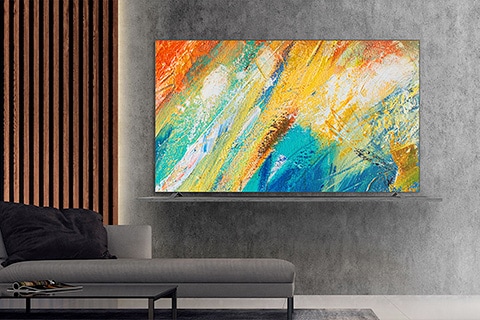 Sala de estar moderna com uma TV de tela plana montada na parede exibindo uma pintura abstrata colorida, posicionada acima de um sofá cinza.