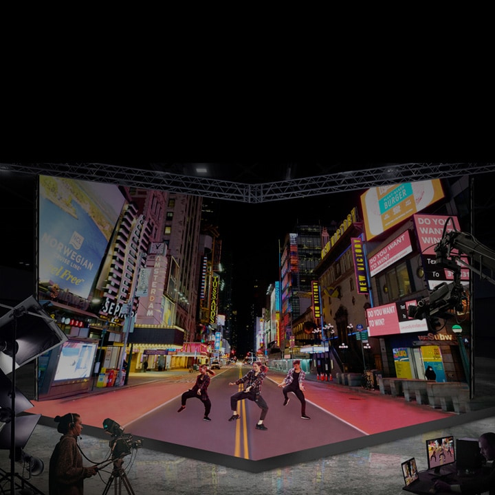 Studio avec grand écran à DEL incurvé affichant une scène urbaine animée la nuit. Des artistes dansent devant l’écran pendant qu’un cameraman enregistre la scène, simulant un environnement urbain extérieur à l’intérieur.
