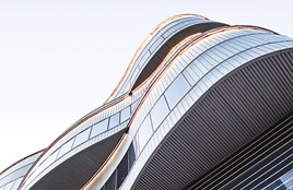 Modernes Glasgebäude mit geschwungener Architektur, von unten betrachtet.