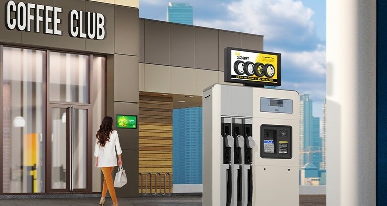 Werbung für Reifen wird auf einem 22XE1J angezeigt, der am oberen Teil des Gasölerators installiert ist. Eine Dame, die ein Café betritt, sieht sich die Werbung auf dem 22XE1J an, der an der Gebäudewand installiert ist.