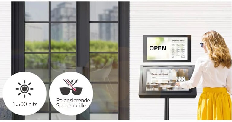 Ein 22XE1J ist an der Wand am Eingang des Gebäudes installiert, darunter steht ein weiterer 22XE1J für die Reservierung. Die Dame mit Sonnenbrille benutzt den 22XE1J-Bildschirm mit einem Touch-Overlay, um eine Reservierung vorzunehmen. Der Bildschirm bleibt auch bei direkter Sonneneinstrahlung sichtbar.