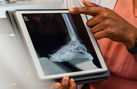 A healthcare professional shows a foot and ankle X-ray on a tablet.