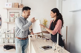 A smiling customer receives a shopping bag from a female shop assistant across the counter in a boutique.