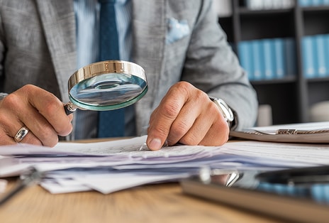 Hands reviewing documents with a magnifying glass representing ethics and compliance management