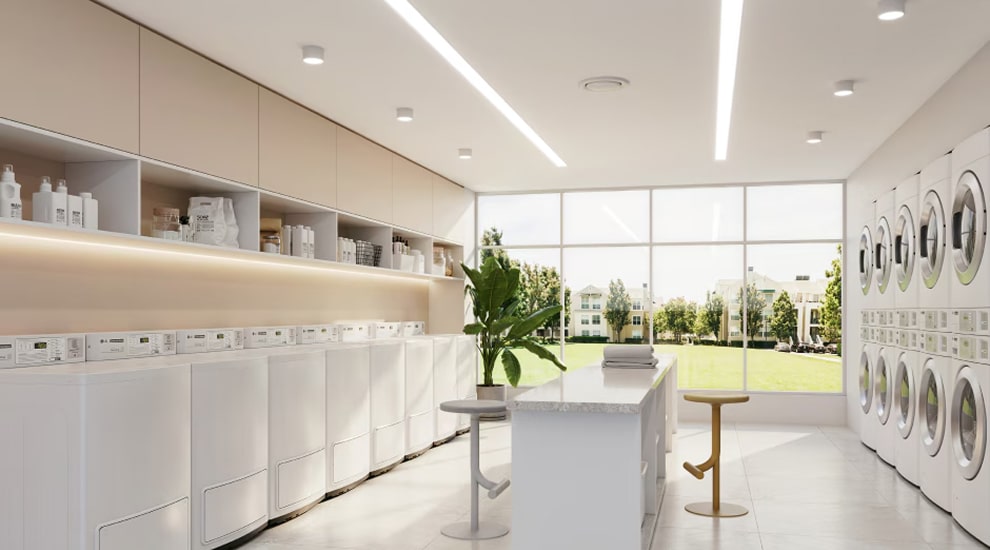 Modern on-premises laundry room with LG commercial washers and dryers, central folding table, and large windows with garden view