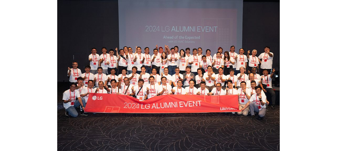 Group of people posing for a photo at the 2024 LG Alumni Event, holding a banner that reads '2024 LG Alumni Event' in front of a presentation screen.