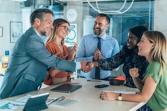Business team meeting with diverse professionals smiling, shaking hands, and celebrating success in a modern office environment