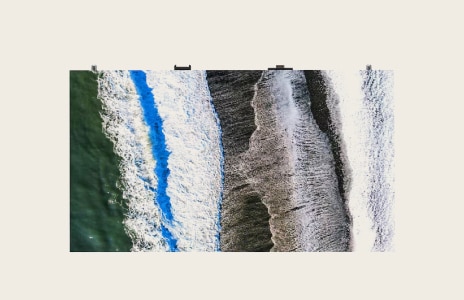 Aerial drone shot of ocean waves crashing on the shore, creating contrasting blue and white foam textures – beach and coastal photography.