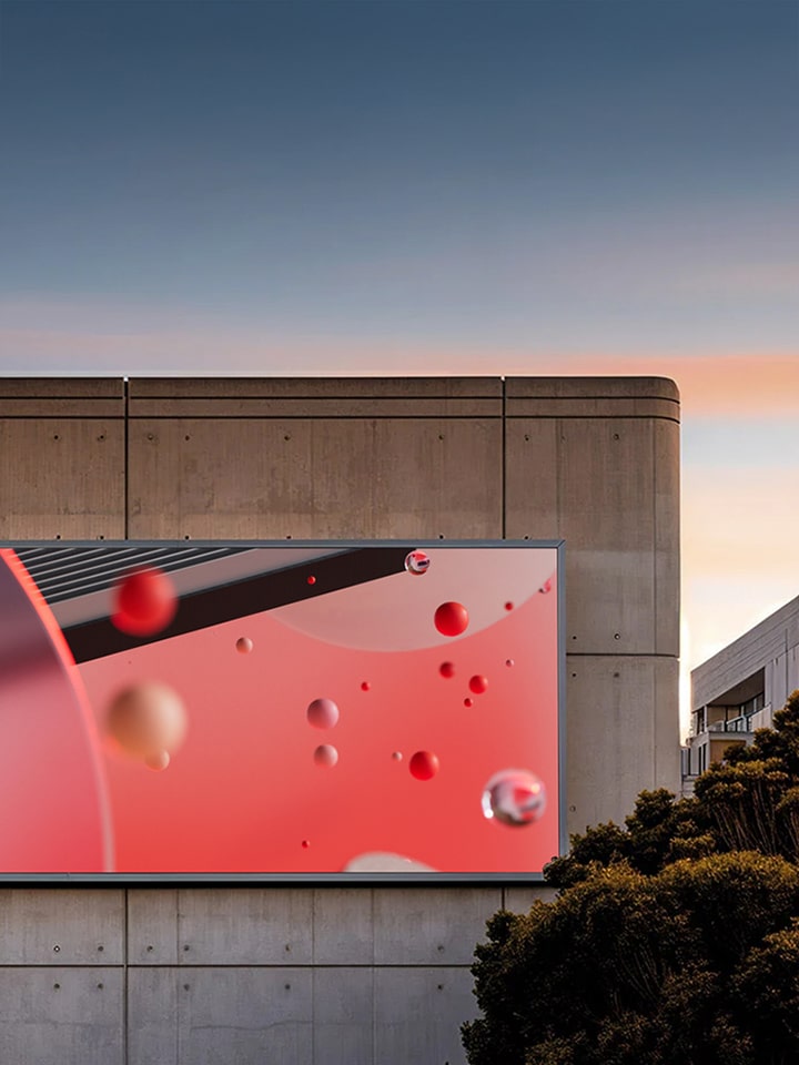 A large digital billboard on a concrete building displays abstract red and black visuals with floating 3D spheres.