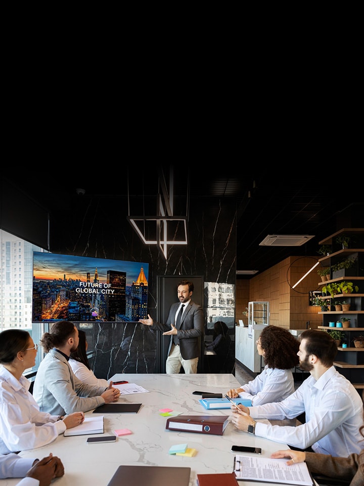 LG Information Display training session shows a presenter using a large LG signage screen to brief a business team inside a modern conference room