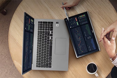 Overhead view of a laptop on a round table with two foldable extended screens showing charts and data, with a cup of coffee nearby