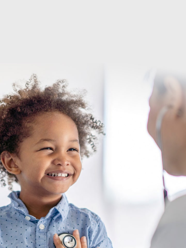 A smiling child during a medical checkup as a female doctor holds a stethoscope.