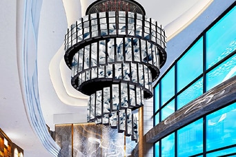 Luxury hotel lobby featuring a crystal chandelier, marble finishes and floor-to-ceiling windows, showcasing contemporary architecture and design.