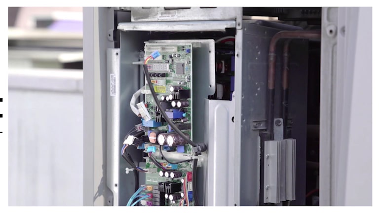 Wearing gloves, a person extracts a component, entwined with complex wiring, from a rectangular metallic box.