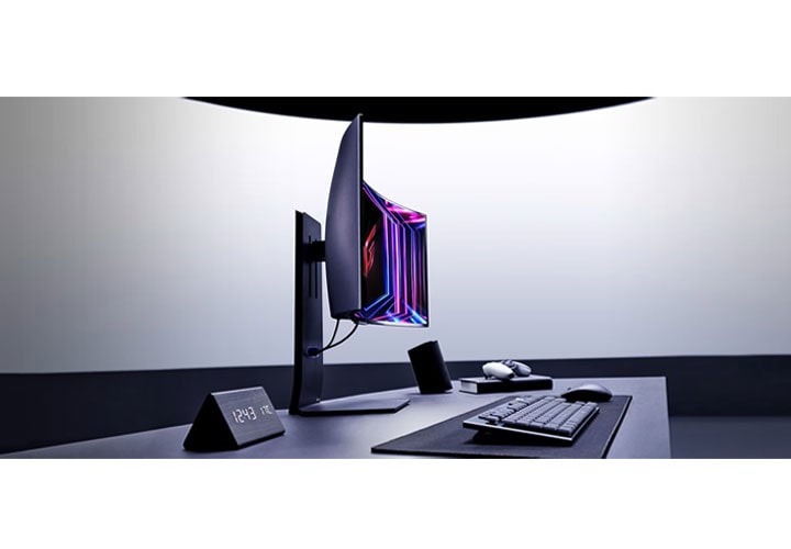 Uma configuração de desktop moderna apresenta um monitor de jogo curvo LG com cores vibrantes, um teclado, um mouse e um relógio inclinado exibindo o tempo. A configuração é minimalista e profissional.