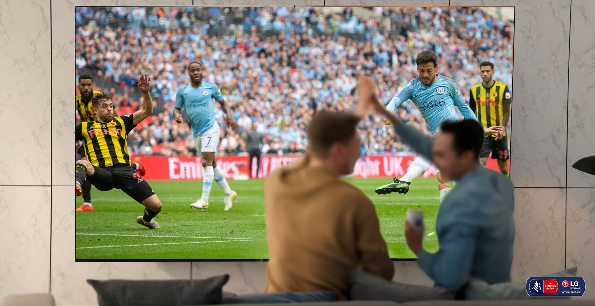 Zwei Männer jubeln, während sie sich im Wohnzimmer auf einem NanoCell TV ein Fussballspiel ansehen. Darunter wird dargestellt, wie die NanoCell-Technologie die Bildqualität verbessert.