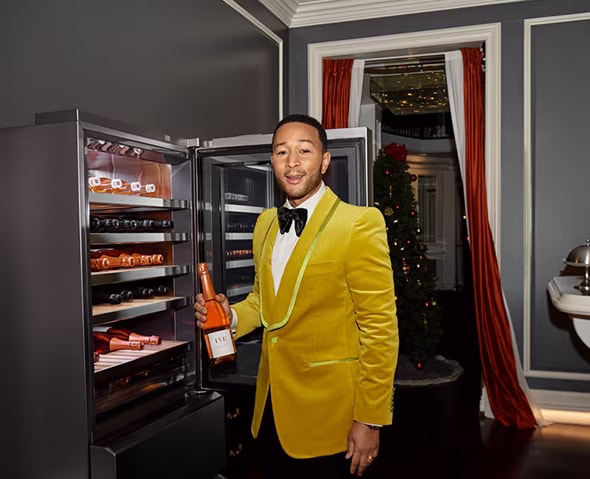 El cantante John Legend posando mientras sostiene una botella de vino frente a una bodega LG SIGNATURE.