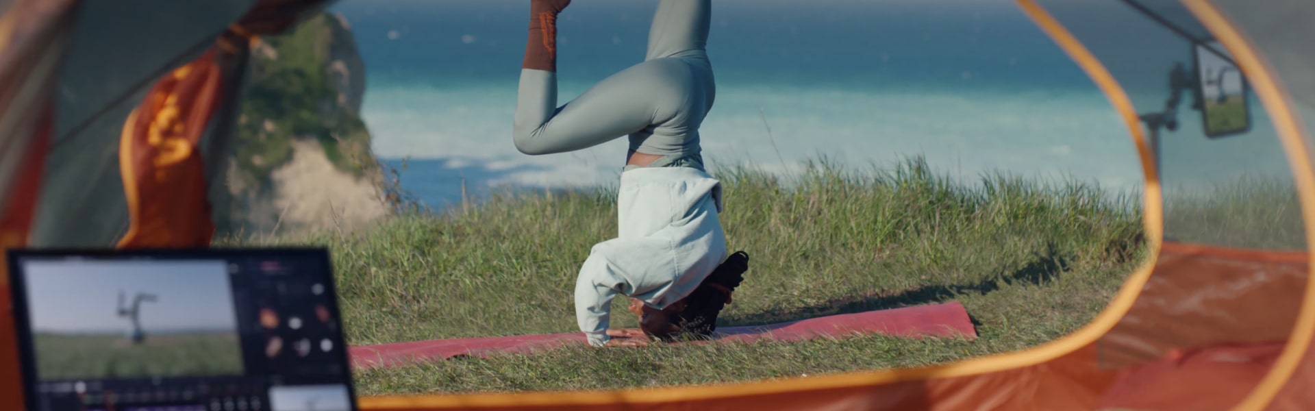Une femme faisant le poirier sur un tapis de yoga au bord de l'océan, filmant avec son smartphone affiché sur un LG Gram.