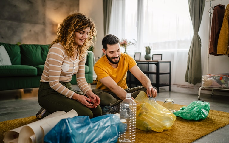 Couple separating recyclable materials (plastic bag, plastic bottle and paper)