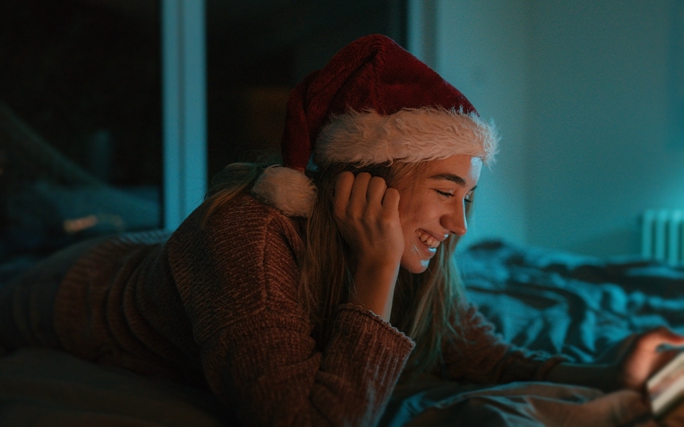 A girl smiling at her smartphone whilst wearing a Christmas hat