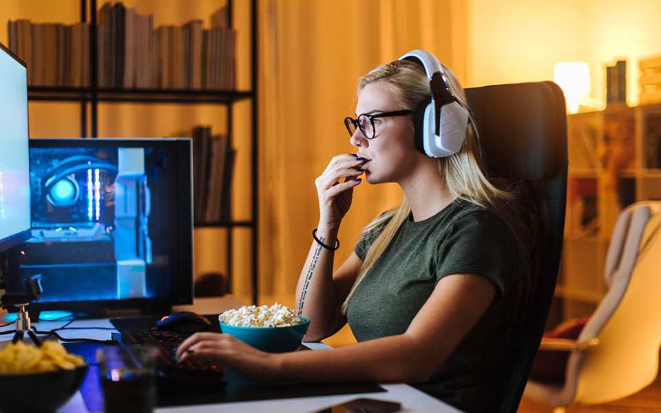 A woman eating popcorn and wearing headphones whilst working on her computer. 