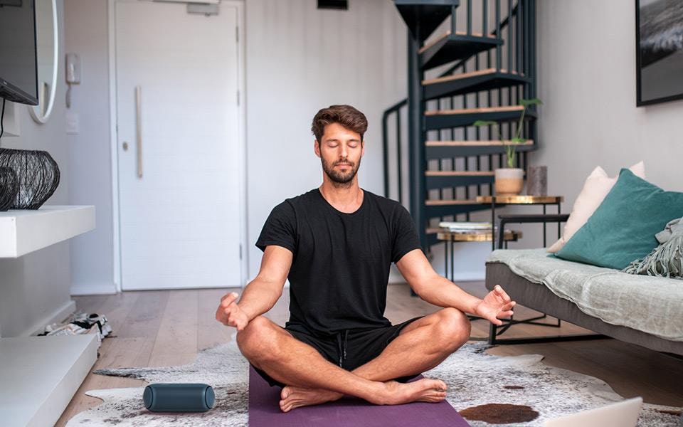 A man meditating in a living room with an LG XBOOM Go speaker