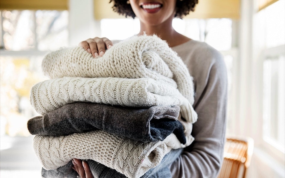 A smiling woman carries a stack of soft winter sweaters and blankets to her LG washing machine