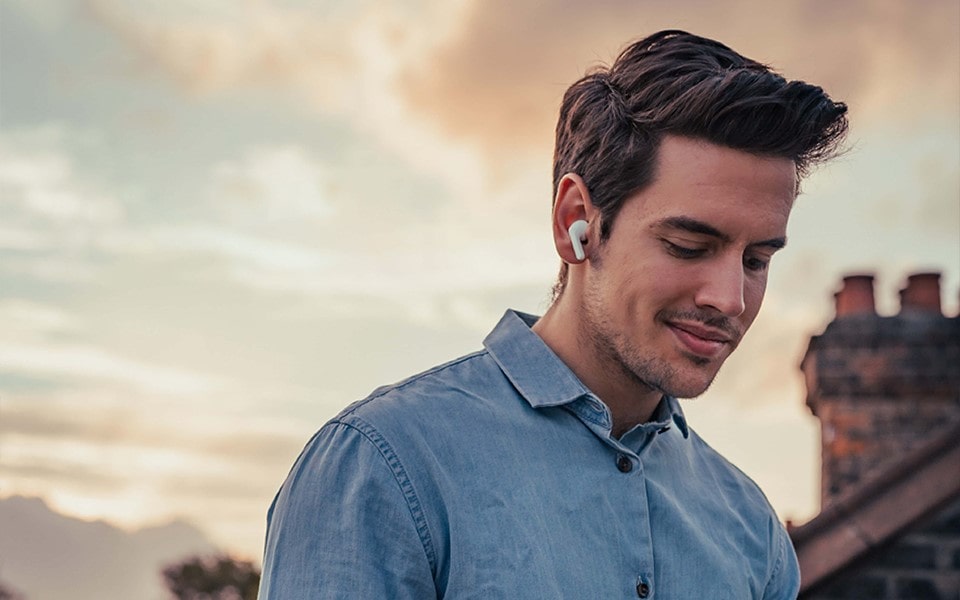 A young man is outside using sound earbuds