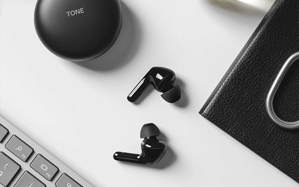 A pair of black earbuds lay on a desk with a matching charging cradle nearby