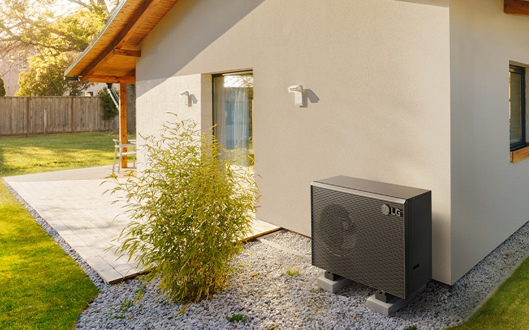 Therma V R290 Monobloc Heat Pump installed in a garden beside a house wall, showcasing its sleek design and functionality.