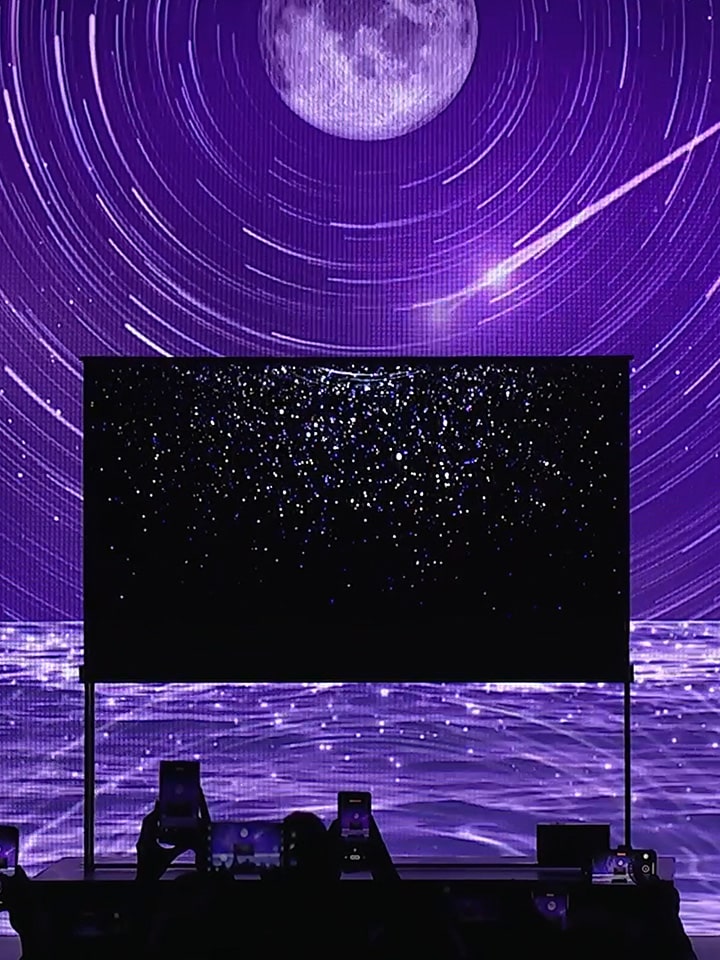 Behind the LG SIGNATURE OLED T, which shows starlight on the background screen, there is a sea, moon, and stars shining in purple as the background.