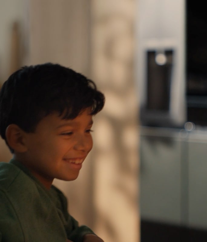 The child's face is clearly visible in front of the candlelit cake, and the LG InstaView refrigerator is faintly visible in the background. 