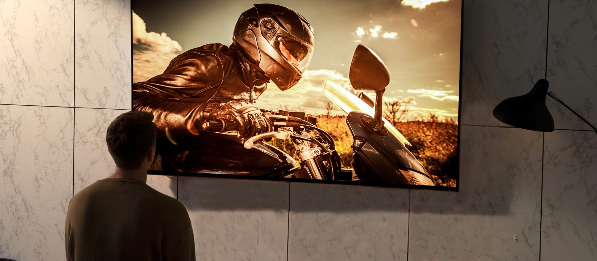 La parte de atrás de un hombre mirando la televisión en la pared de la sala de estar. Hay una escena de una película de motos en la pantalla.