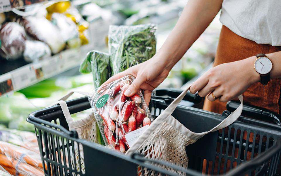 A woman placing vegetables in a shopping basket at the grocery store