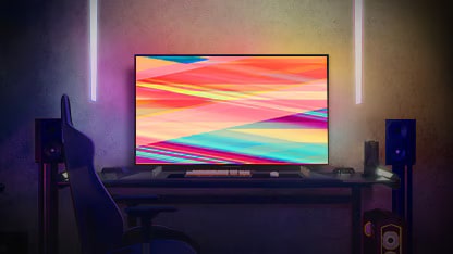 LG OLED C2 staat 's avonds in een warm verlichte kamer met banken, veel kussens, een lamp, een bijzettafeltje en een plant